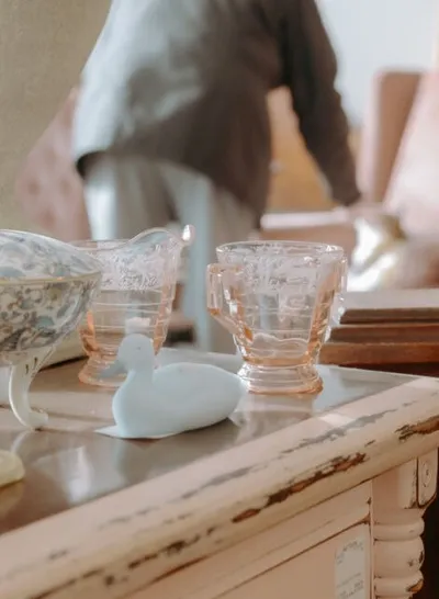 Pink depression glass cups and a white ceramic bird figurine on a chippy painted dresser