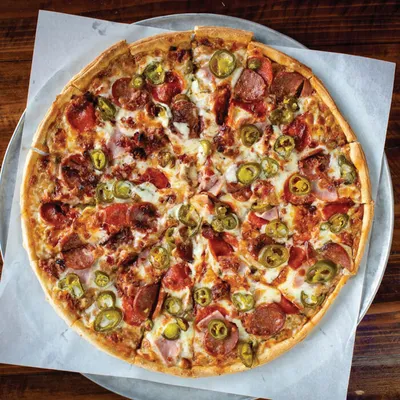 Whole pizza topped with pepperoni, sliced jalapeños, ham, and melted cheese on parchment