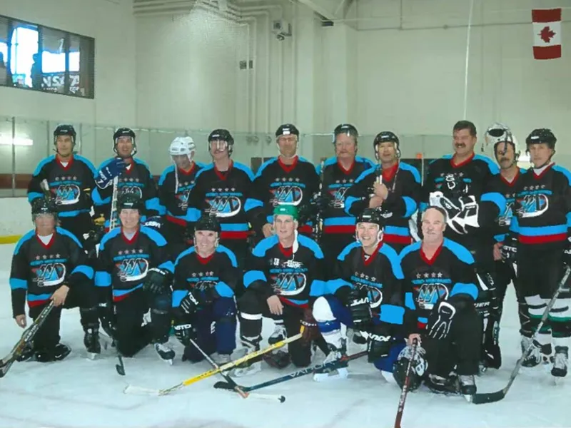 Hockey team in matching black and teal jerseys posing together on an indoor rink