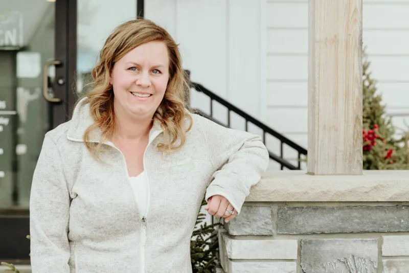 Smiling woman in a grey zip-up fleece leaning against a stone pillar outside a building