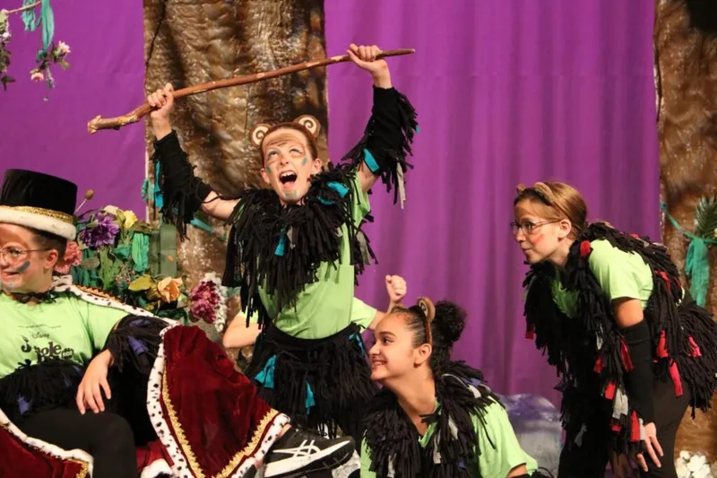 Children in monkey costumes and face paint perform energetically on a colorful theatrical stage