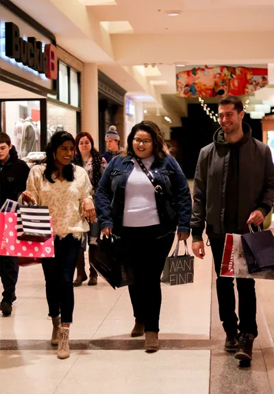 Shoppers carrying bags walk through a busy indoor mall corridor