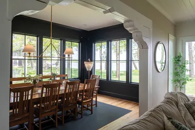 Dining room with long wooden table, pendant lights, and dark walls framing lake views