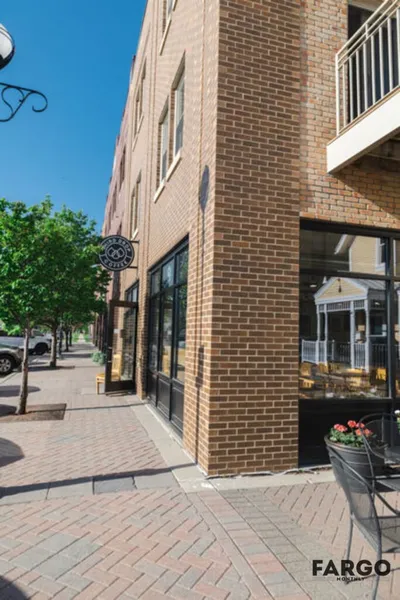Brick corner building with storefront windows and a small patio on a sunny downtown street
