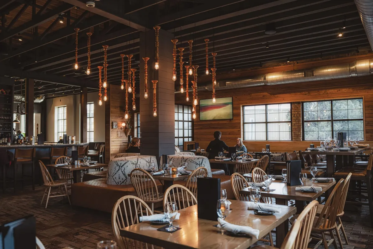 Warmly lit restaurant dining room with Edison bulb pendants, wood walls, and set tables