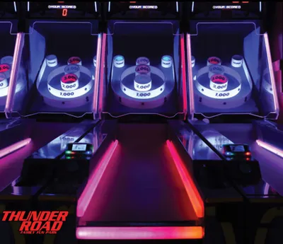 Row of glowing skee-ball arcade lanes with neon pink and purple lighting