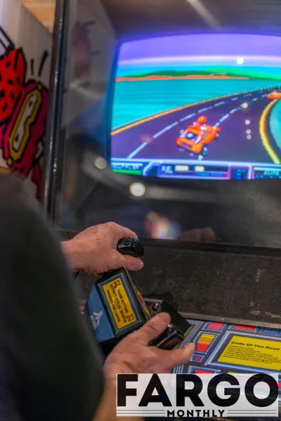 Person gripping a joystick on a vintage racing arcade cabinet with colorful screen