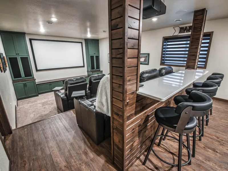 Home theater room with black recliner seats, large projection screen, green built-in cabinets, and a bar counter with black