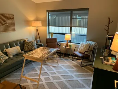 Cozy therapy office with gray sofa, leather chairs, floor lamp, and puzzle on a wooden tray table