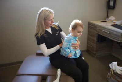 Female chiropractor in black scrubs examining a toddler on a treatment table