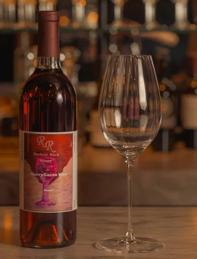 Rookery Rock Winery Cherry-Cocoa Wine bottle beside an empty wine glass on a wooden bar