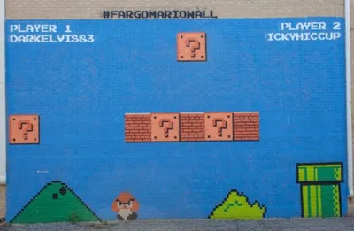 Outdoor brick wall mural painted as a Super Mario Bros. level scene with pixel-art characters and blocks