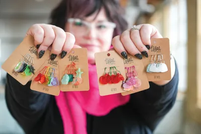 Woman holding four kraft card earring sets featuring colorful handmade fiber tassels and charms