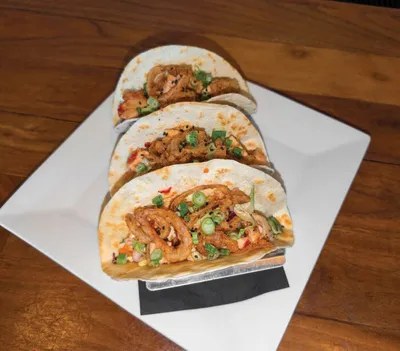 Three shrimp tacos with green onions and red peppers on a white plate