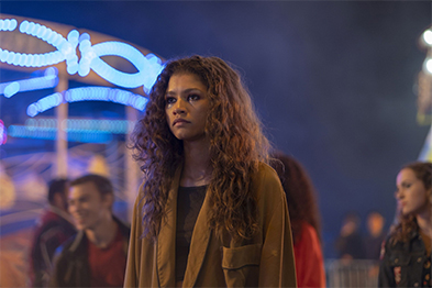 Young woman with curly hair in an olive jacket at a lit-up fairground at night