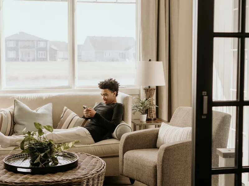 Young man relaxing on a beige sofa scrolling his phone in a bright living room