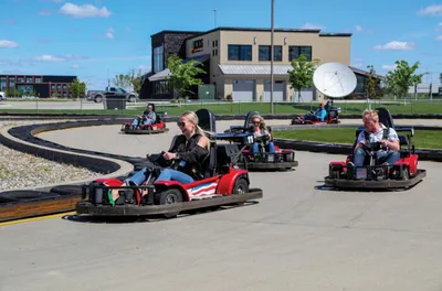 Adults racing go-karts on an outdoor paved track on a sunny day