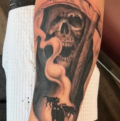 Black and grey tattoo of a hooded grim reaper skull with small black cats below