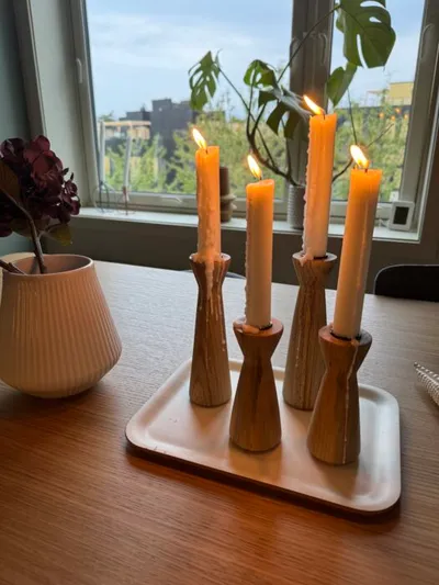 Four lit taper candles in wooden handcrafted holders on a white tray atop a wood table