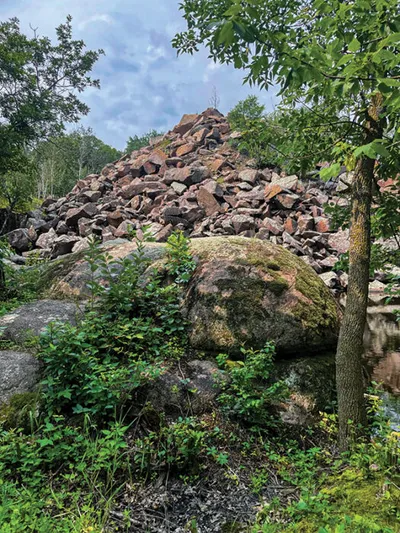 Large pyramid-shaped pile of reddish granite boulders surrounded by trees and low shrubs