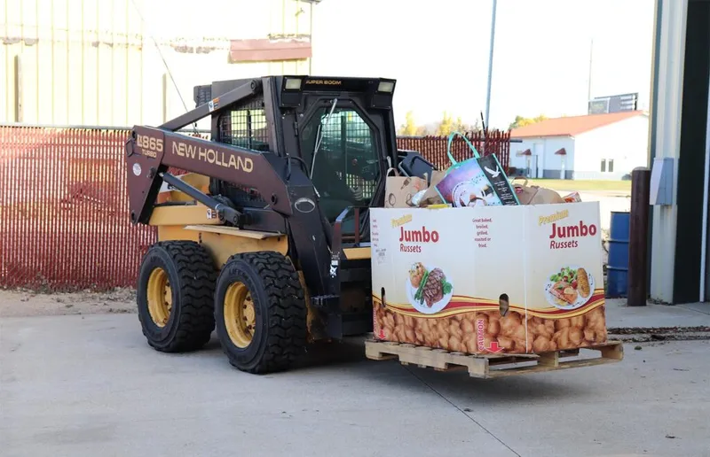 New Holland skid steer loader carrying a pallet of Jumbo Russets potato boxes