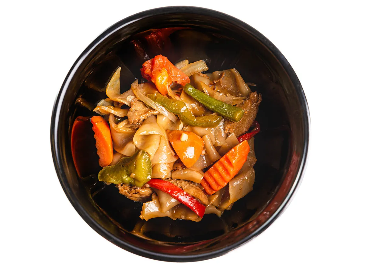Stir-fried flat rice noodles with carrots, bell peppers, and meat in a dark bowl