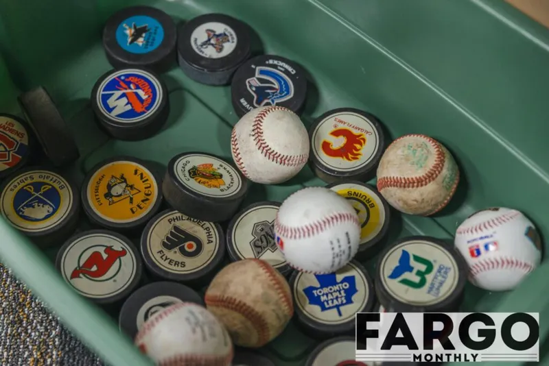 Green bin filled with NHL-logo hockey pucks and worn baseballs