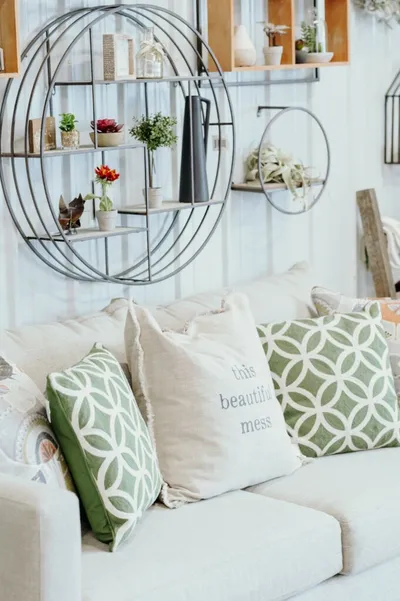 White sofa with green patterned and linen pillows below circular metal wall shelves holding small potted plants