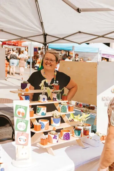 Smiling woman behind a wooden display shelf of colorful painted pots at an outdoor market