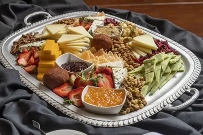 Silver serving tray with cheese, strawberries, nuts, dips, and sliced vegetables