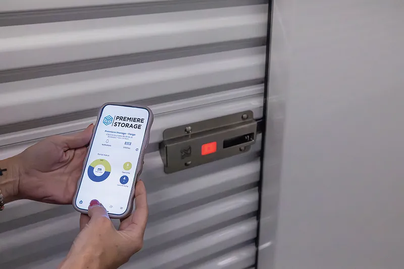 Hand holding a smartphone with a storage app open next to a red-lit electronic lock on a metal roll-up unit door