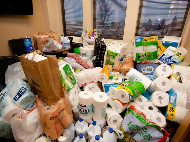 Large pile of paper towels, toilet paper rolls, and cleaning supplies stacked in an office corner