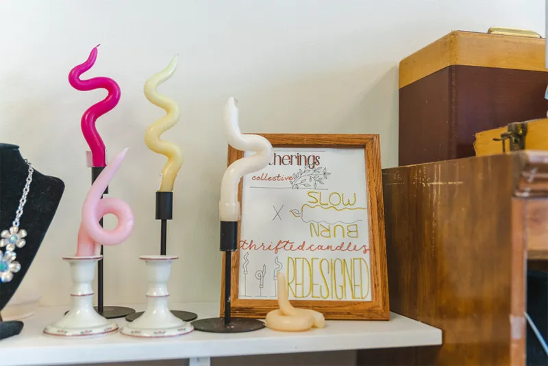 Curvy sculptural candles on candlesticks beside a framed 'Slow Burn' sign on a boutique shelf