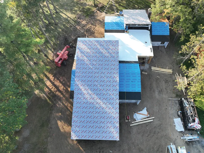 Aerial view of a home under construction with roofing underlayment and blue protective wrap