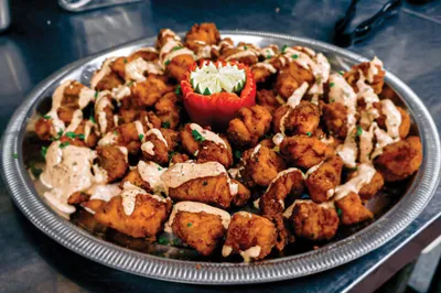 Platter of fried bites drizzled with creamy sauce, centered with a stuffed pepper garnish