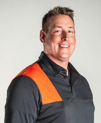 Smiling man in a dark gray and orange athletic polo shirt against a light gray background