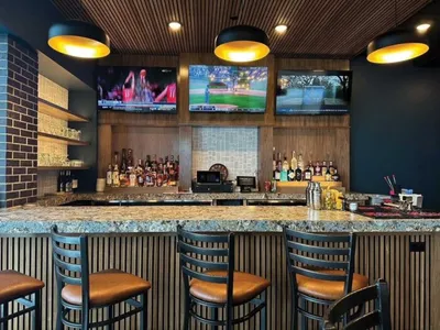 Bar counter with granite top, stools, liquor shelf, and three wall-mounted TVs under pendant lights