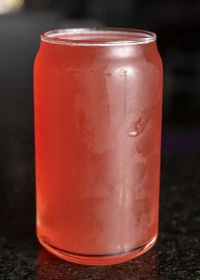 Pink-hued craft drink in a can-shaped glass on a dark surface