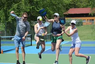 Four adults laughing and posing with pickleball paddles on a bright blue outdoor court
