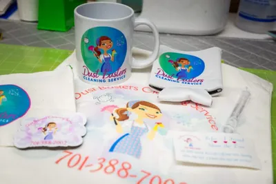 Dust Busters Cleaning Service branded mug, card holder, stickers, and tote displaying the company logo and phone number