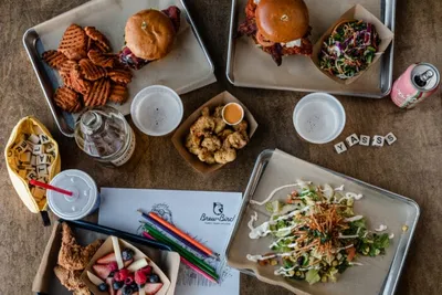 Overhead spread of fried chicken, burgers, waffle fries, and salad on metal trays