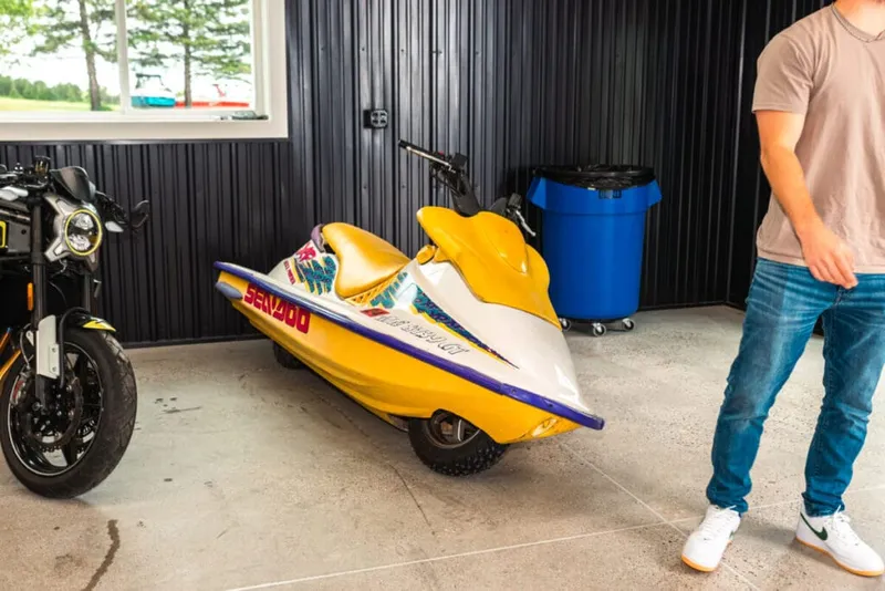 Yellow Sea-Doo personal watercraft on dolly inside a dark-paneled garage beside a motorcycle