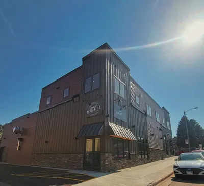 Three-story mixed-use building with dark metal siding and striped awnings under a bright blue sky