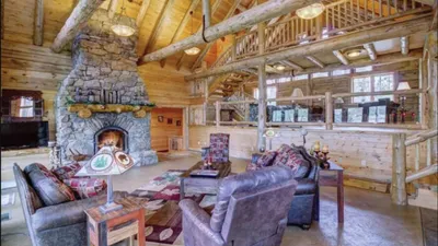 Rustic log cabin living room with stone fireplace, leather sofas, and open loft above