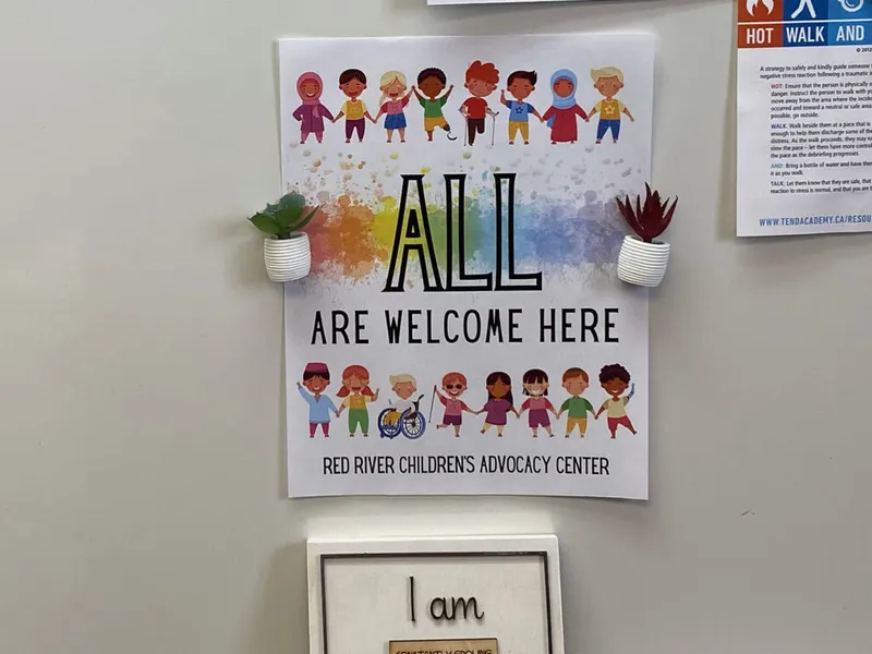 All Are Welcome Here poster from Red River Children's Advocacy Center on a wall