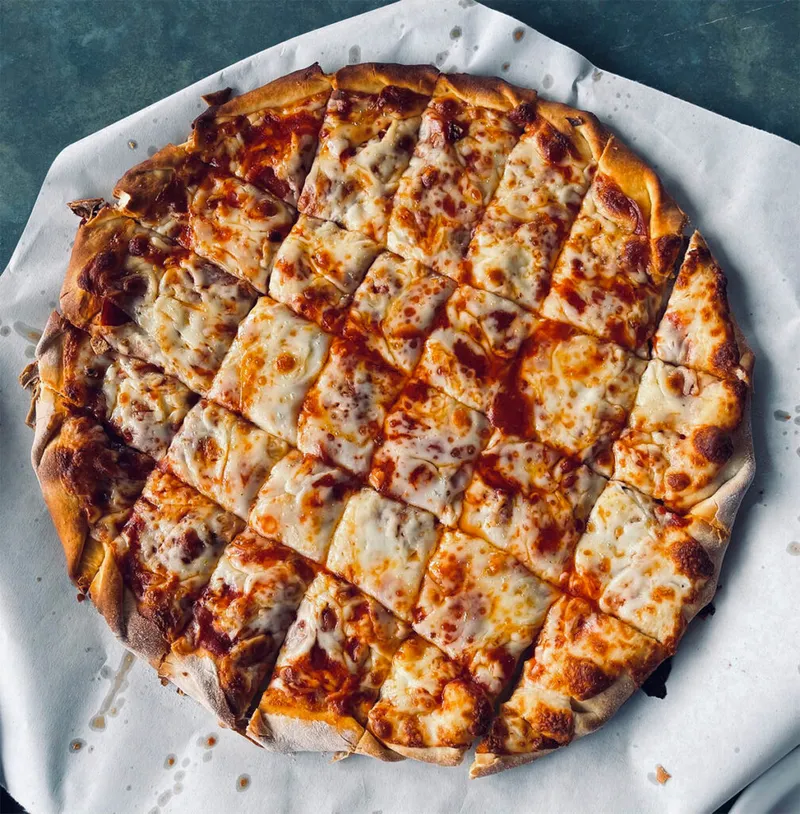 Cheese pizza cut into small squares on white parchment paper