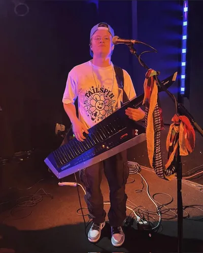 Young musician playing a keytar on a dimly lit stage near a microphone