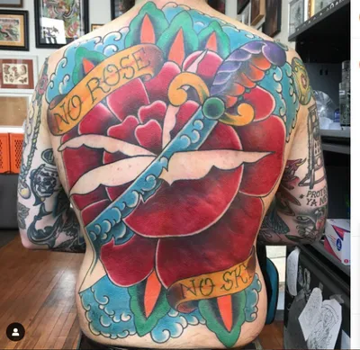 Man's fully tattooed back featuring a large traditional rose with a dagger and banner reading "No Rose No S...
