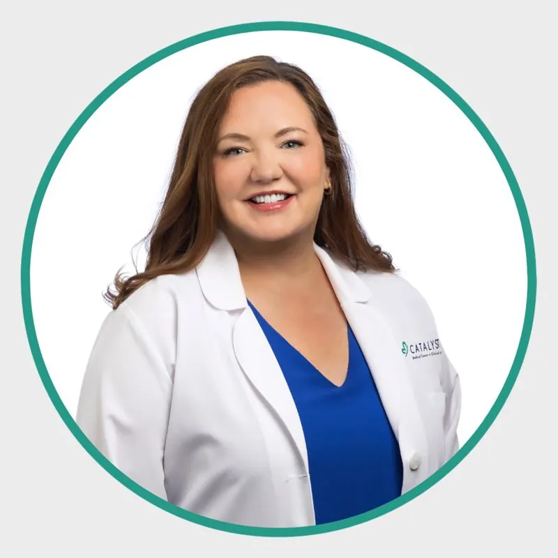 Smiling woman with brown hair in a white lab coat over a blue top
