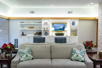 Neutral sofa with green patterned pillows facing built-in white shelving and a framed artwork flanked by red floral